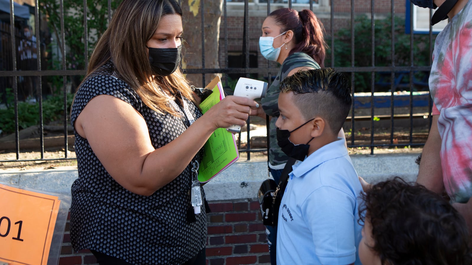 A woman checks a boy’s temperature with a digital thermometer as parents bring their students to school.