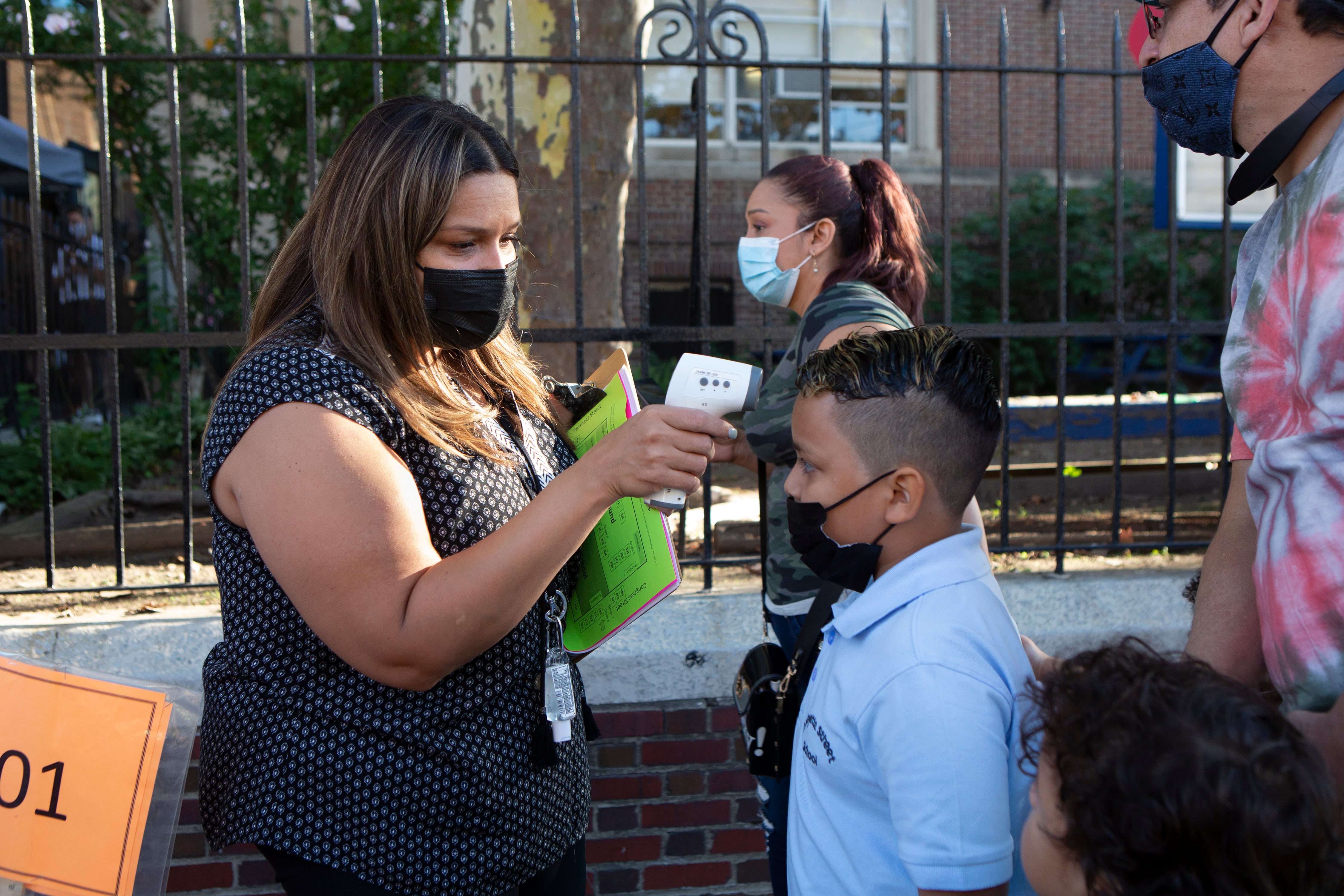 A woman checks a boy’s temperature with a digital thermometer as parents bring their students to school.