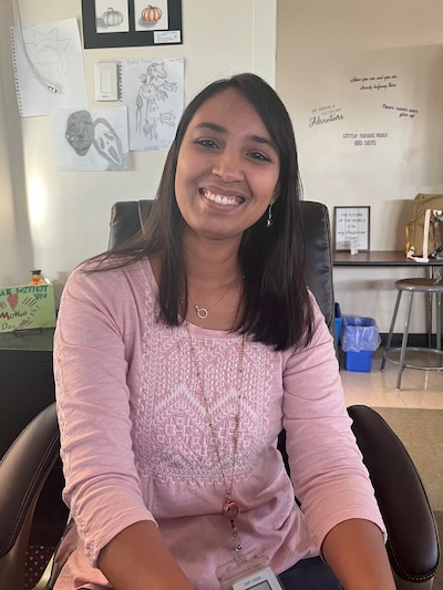 A photograph of a woman with medium-length dark hair and wearing a pink blouse smiles for a self portrait.
