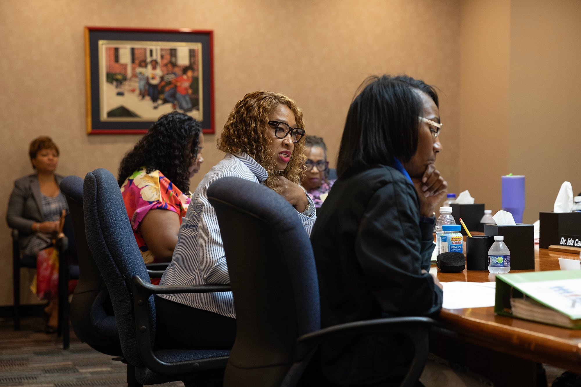 A room full of Black women in business clothes sit around a wooden table in a conference room.