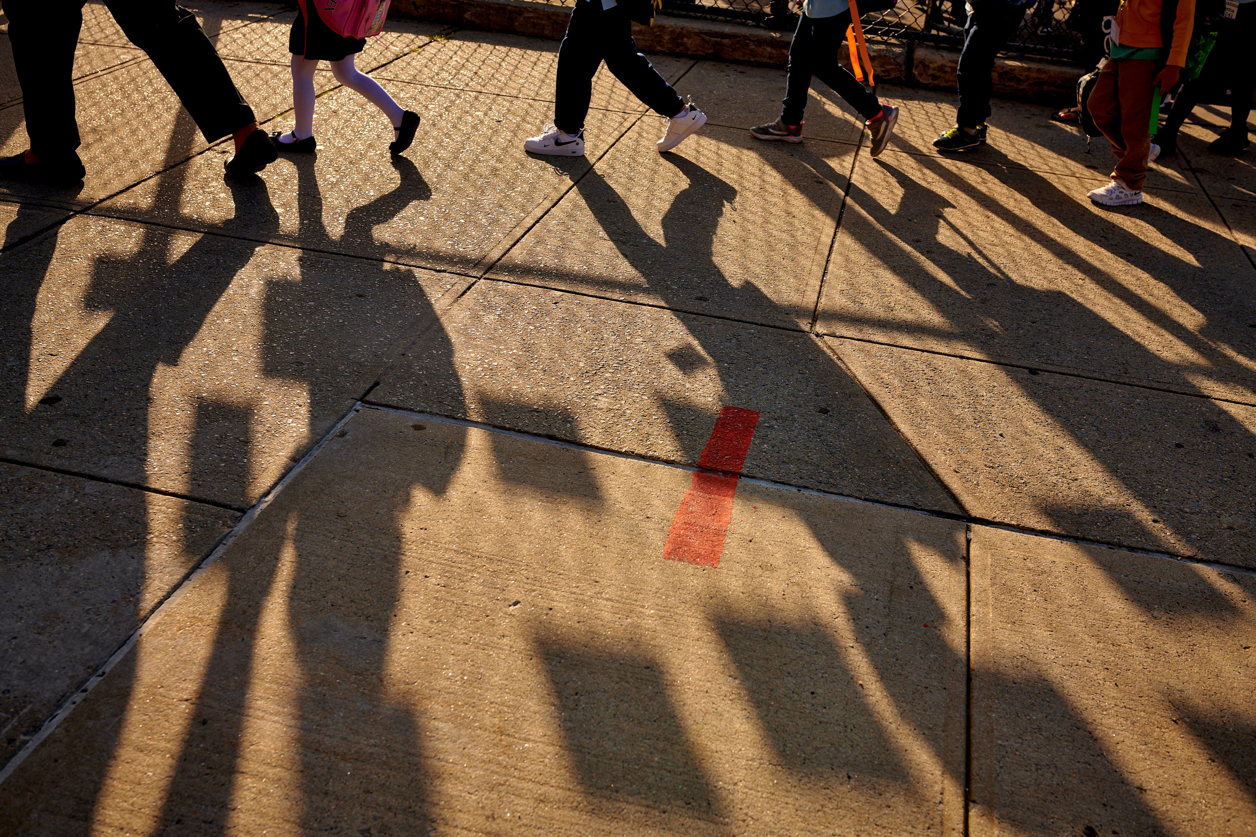 Young students cast long shadows on the sidewalk as they head in for their first day of school.