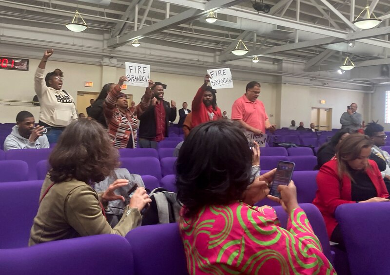 A group of people stand up in a theater seating section holding up signs while others sit in the purple chairs around them.