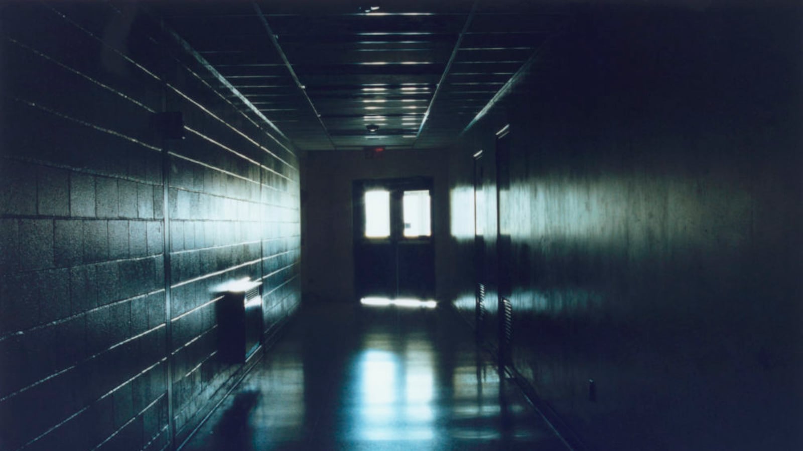 Light comes through a set of double doors at the end of a long, dimly-lit hallway.