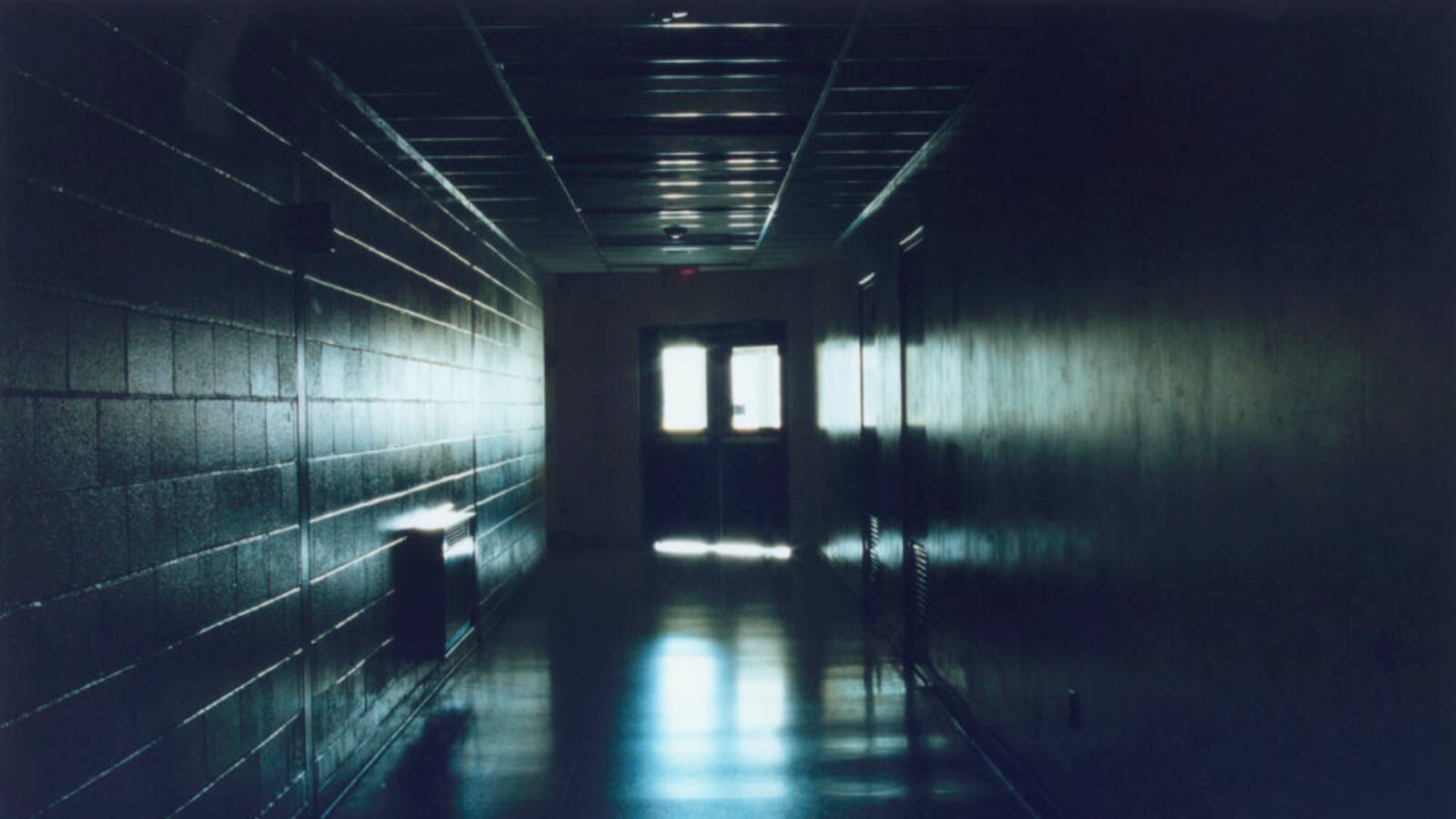 Light comes through a set of double doors at the end of a long, dimly-lit hallway.