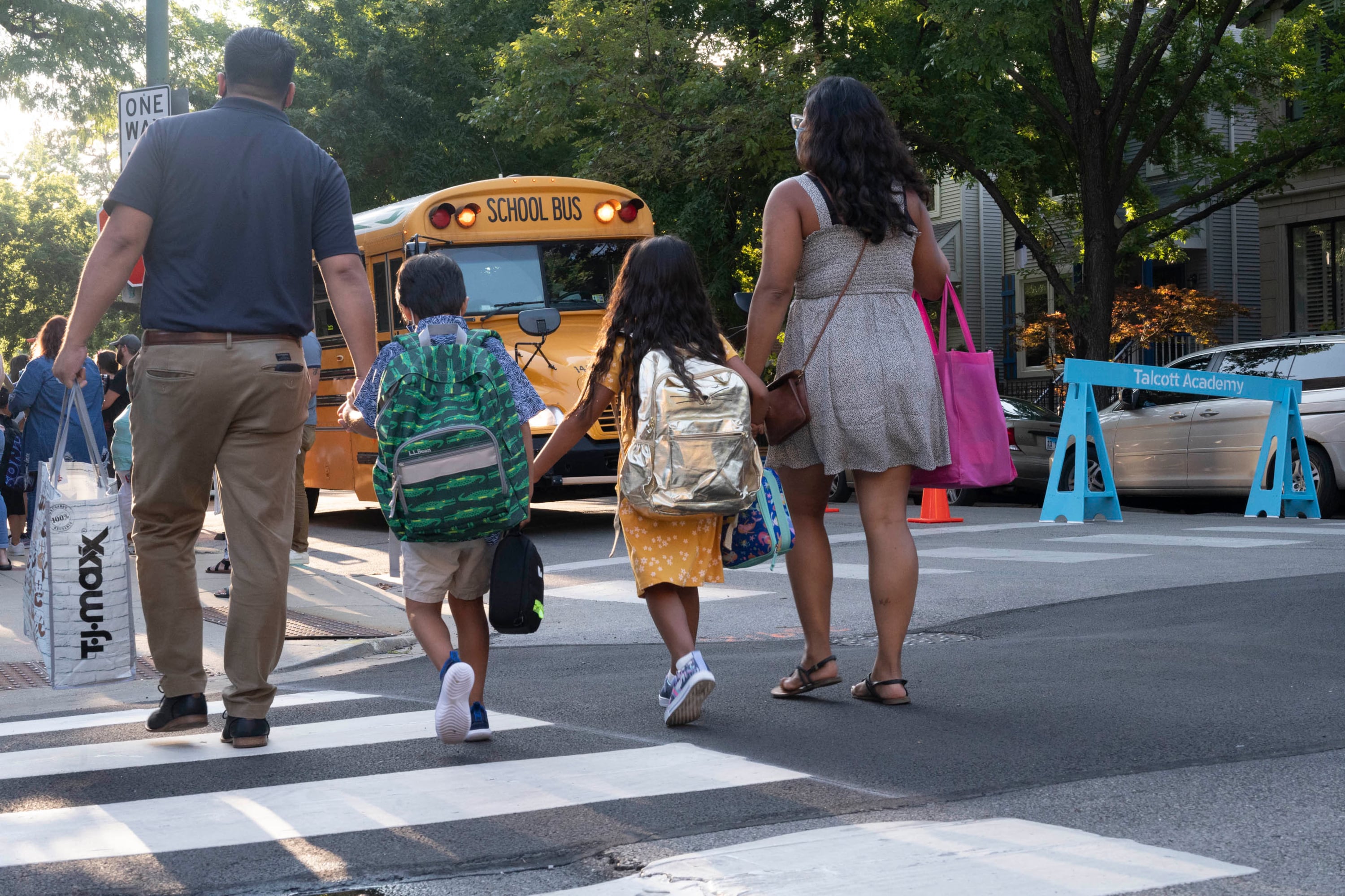 A family of four holds hands as they cross an intersection on the way to their first day of school.