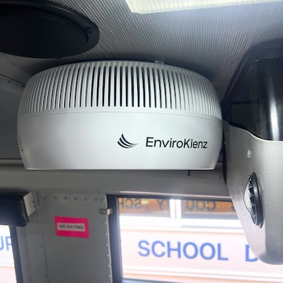 A vented air-cleaning device is attached to the ceiling of a school bus.