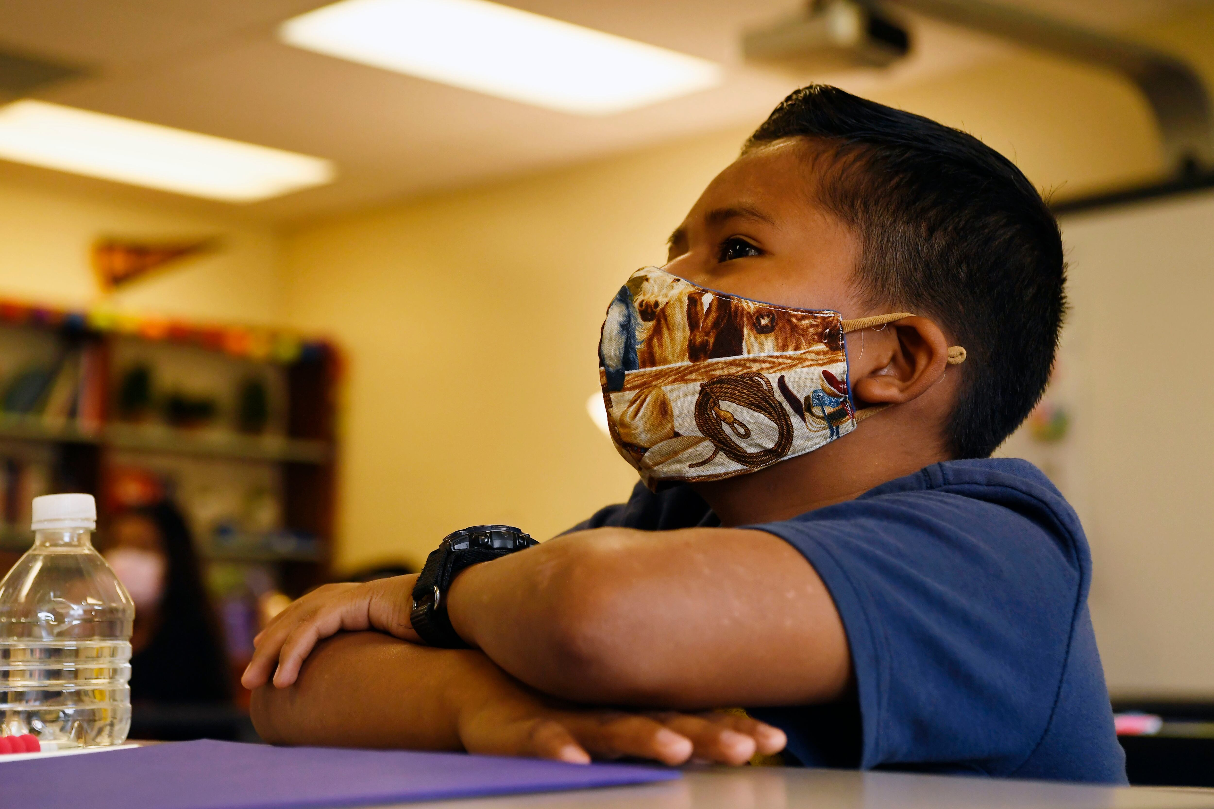 Young boy wearing a mask sits at a desk.