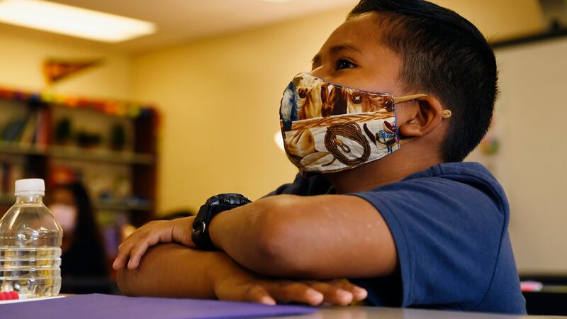 Young boy wearing a mask sits at a desk.