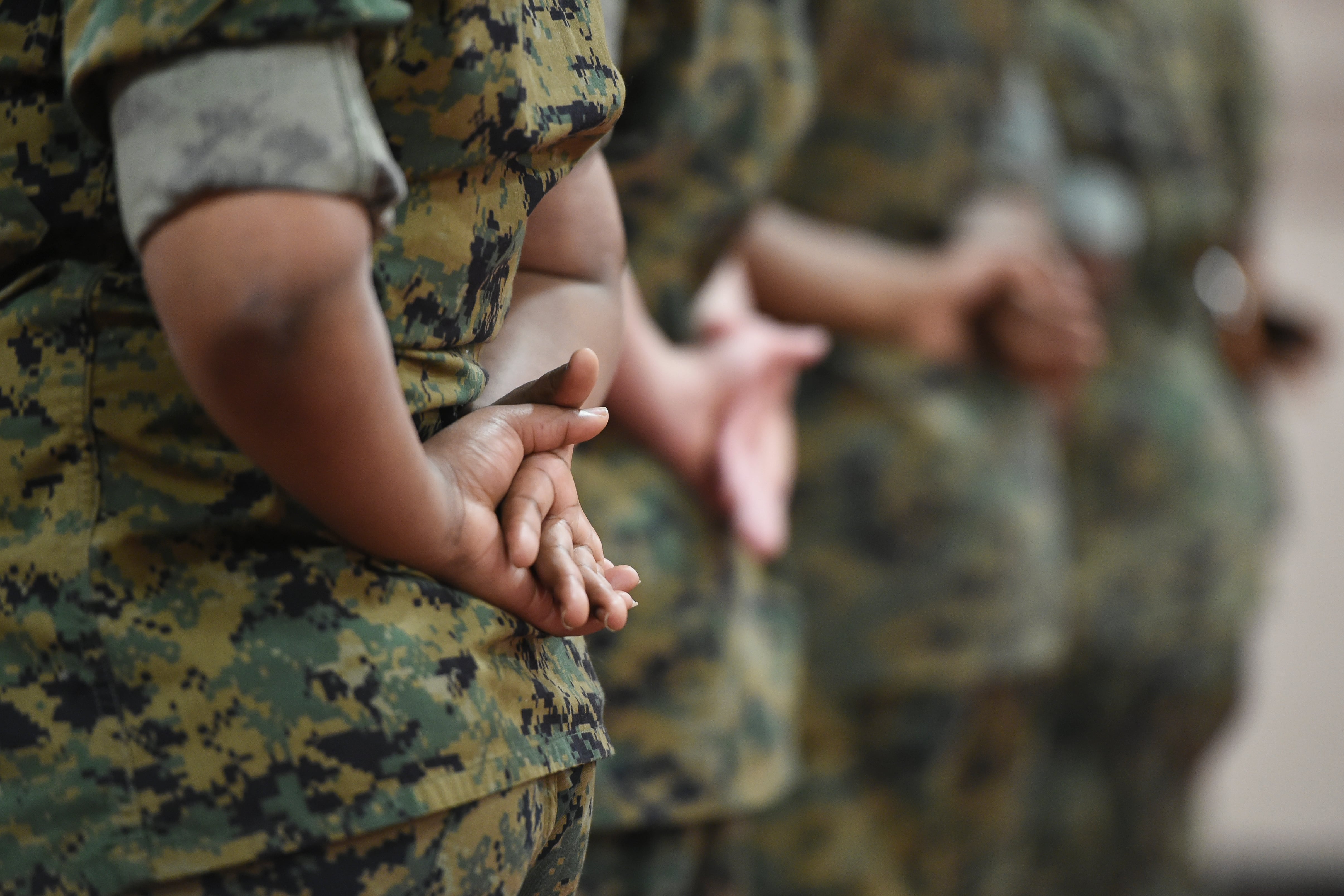 People in military fatigues stand with their hands behind their backs.