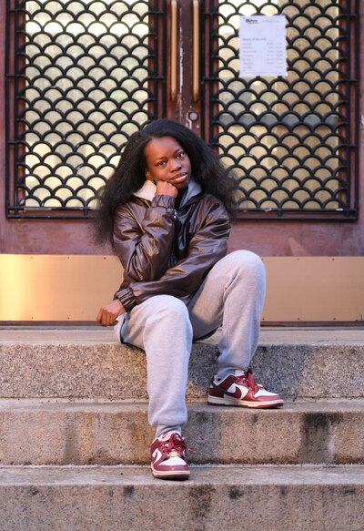 A high school girl with long dark hair and wearing a dark winter jacket sits outside for a portrait.