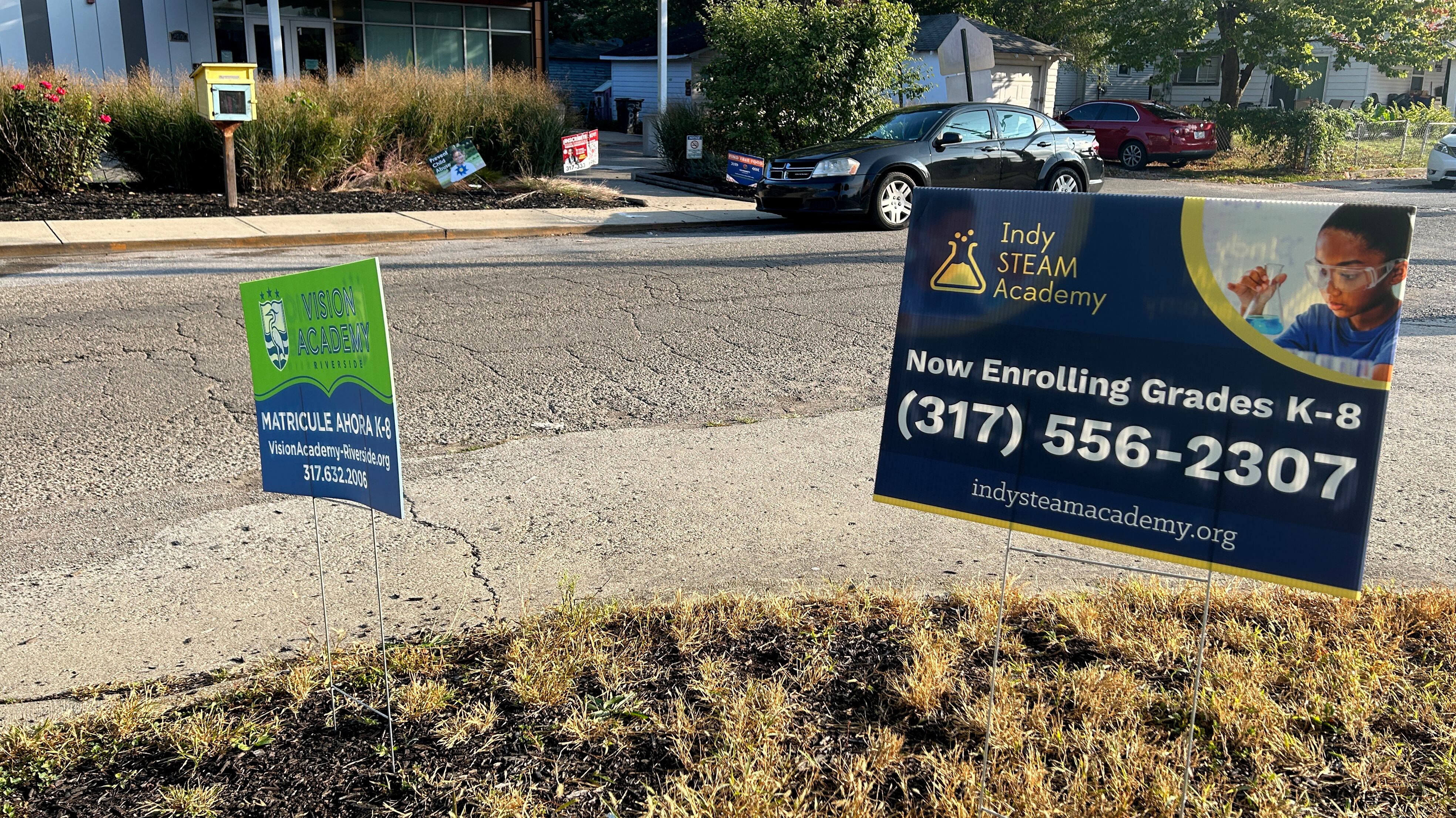 Signs for two schools stand in the ground outside of a building. 