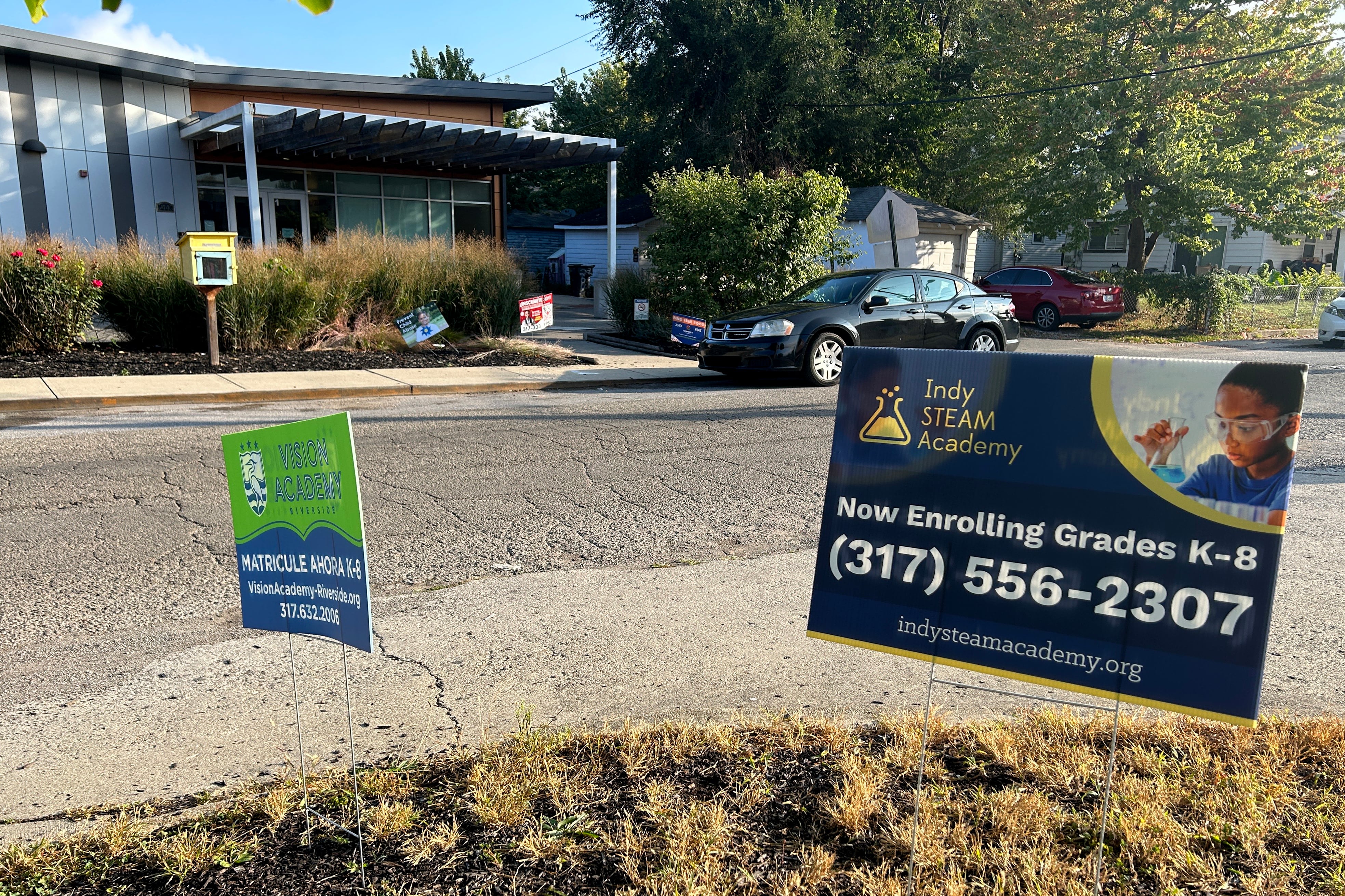 Signs for two schools stand in the ground outside of a building.