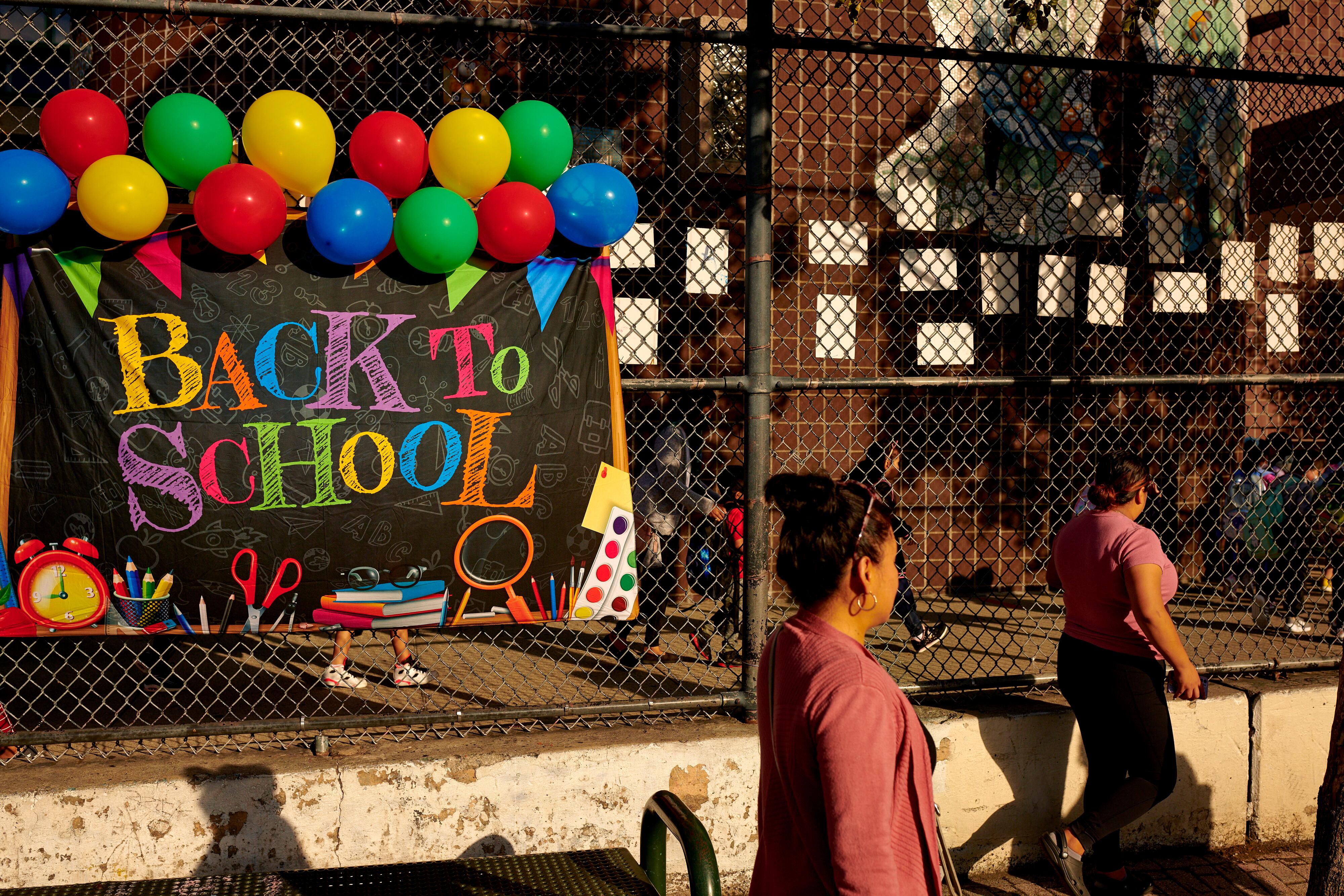 A colorful ‘Welcome back to school’ sign is posted on a fence in front of a brick building.