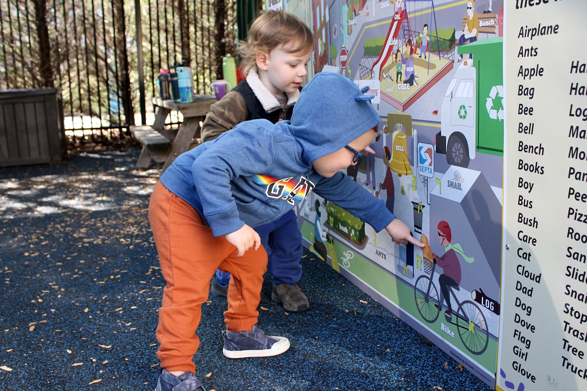 Two young children point to a large picture outside at a playground.