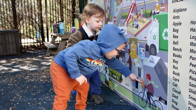 Two young children point to a large picture outside at a playground.
