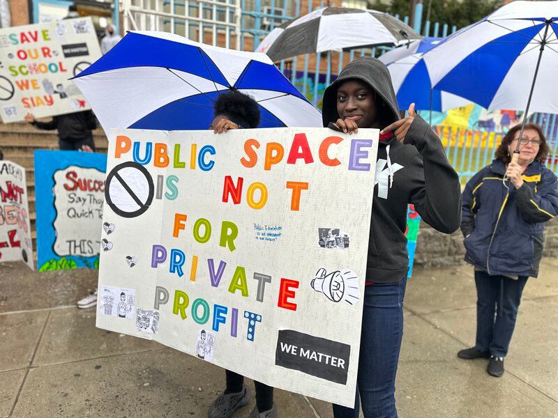 A student holds a sign saying “Public space is not for private profit.”