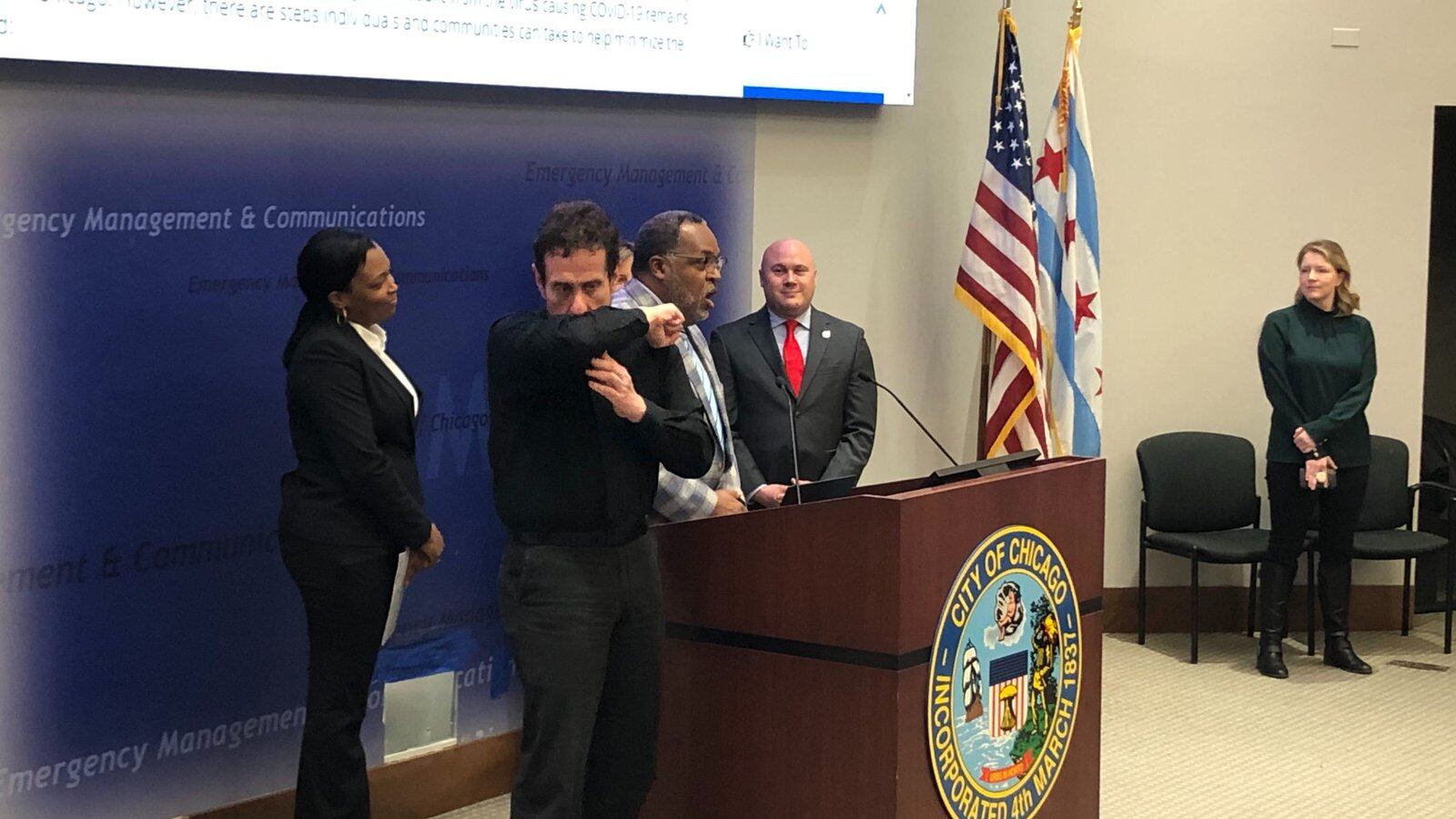 An interpreter demonstrates a proper coughing technique at a Tuesday press conference attended by Chicago schools chief Janice Jackson, left, the district’s Chief Health Officer Kenneth Fox, speaking, and Jennifer Layden, far right, deputy commissioner for the city’s health department.