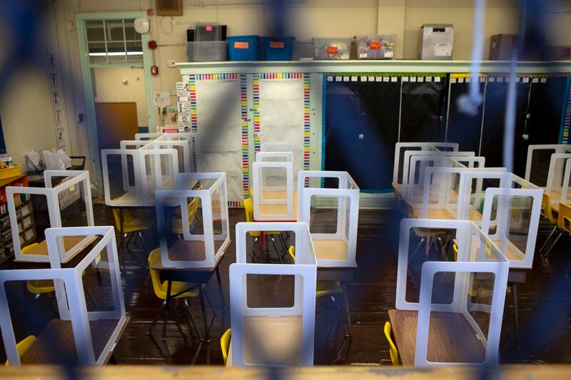 An empty classroom is seen behind a small gate, with plastic barriers on every desk due to COVID concerns.