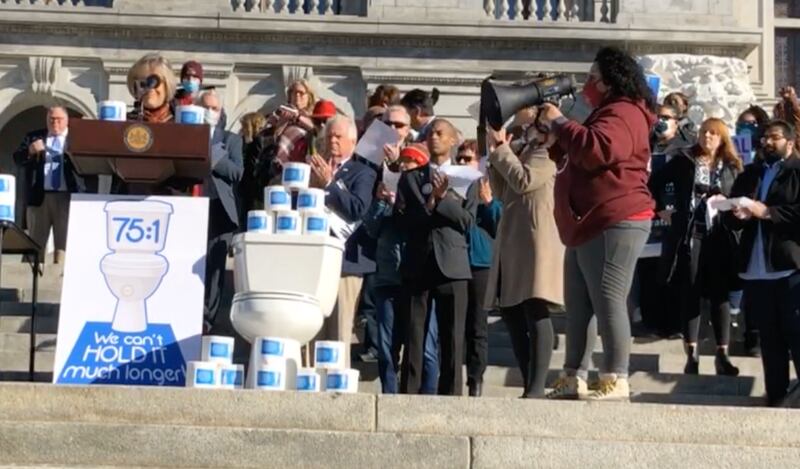 People on the steps of the Pennsylvania Capitol building, with a podium, a toilet and stacks of toilet paper.