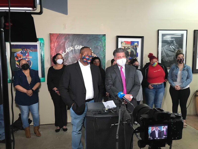 Denver school board member Tay Anderson, left, and his attorney Christopher Decker stand at a podium at a news conference. Supporters stand behind them.