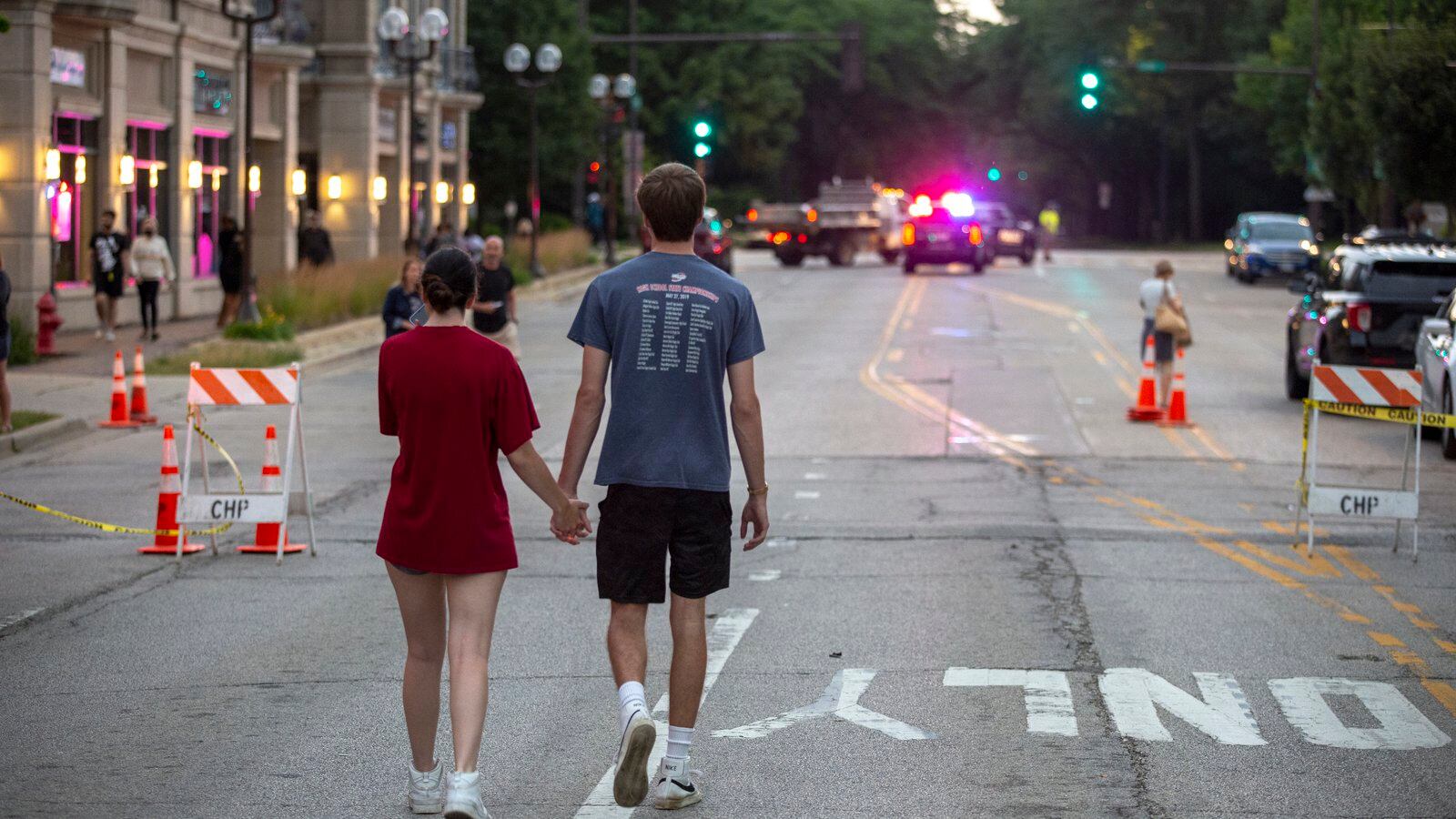 A young couple holding hands walk down the middle of the street in Highland Park, Ill., the road shut down following a mass shooting.