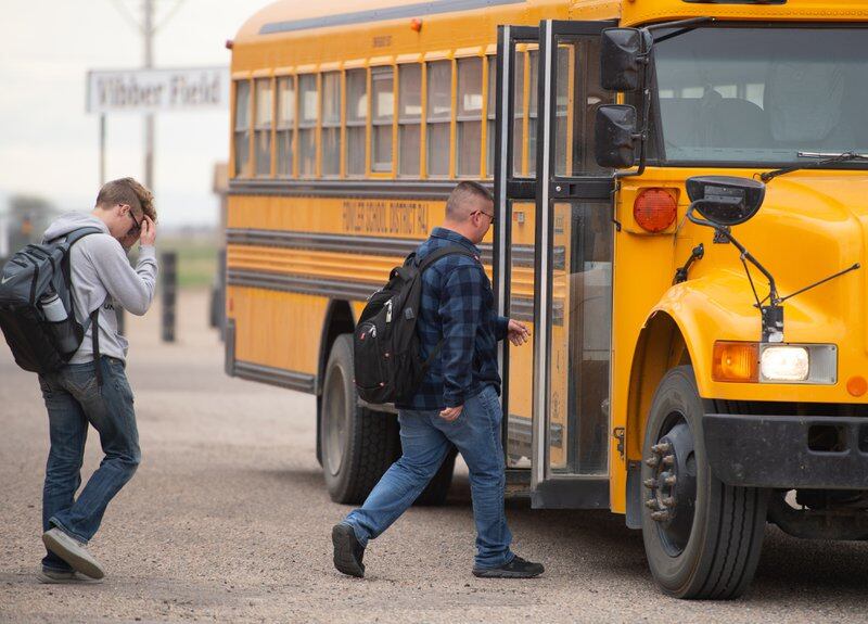 Two teenage boys in jeans and hoodies walk toward a stopped yellow school bus. 