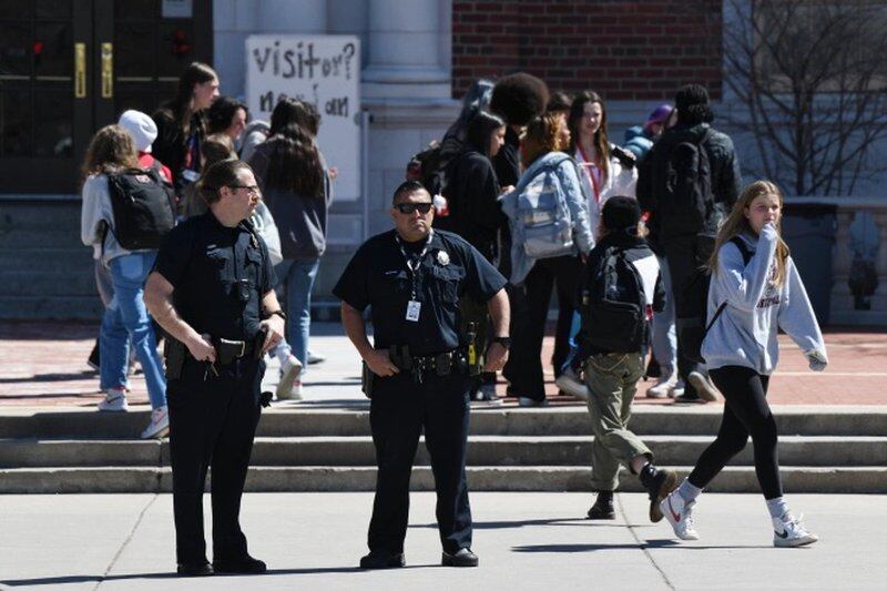 Two police officers stand outside Denver’s East High School as students walk in the background.